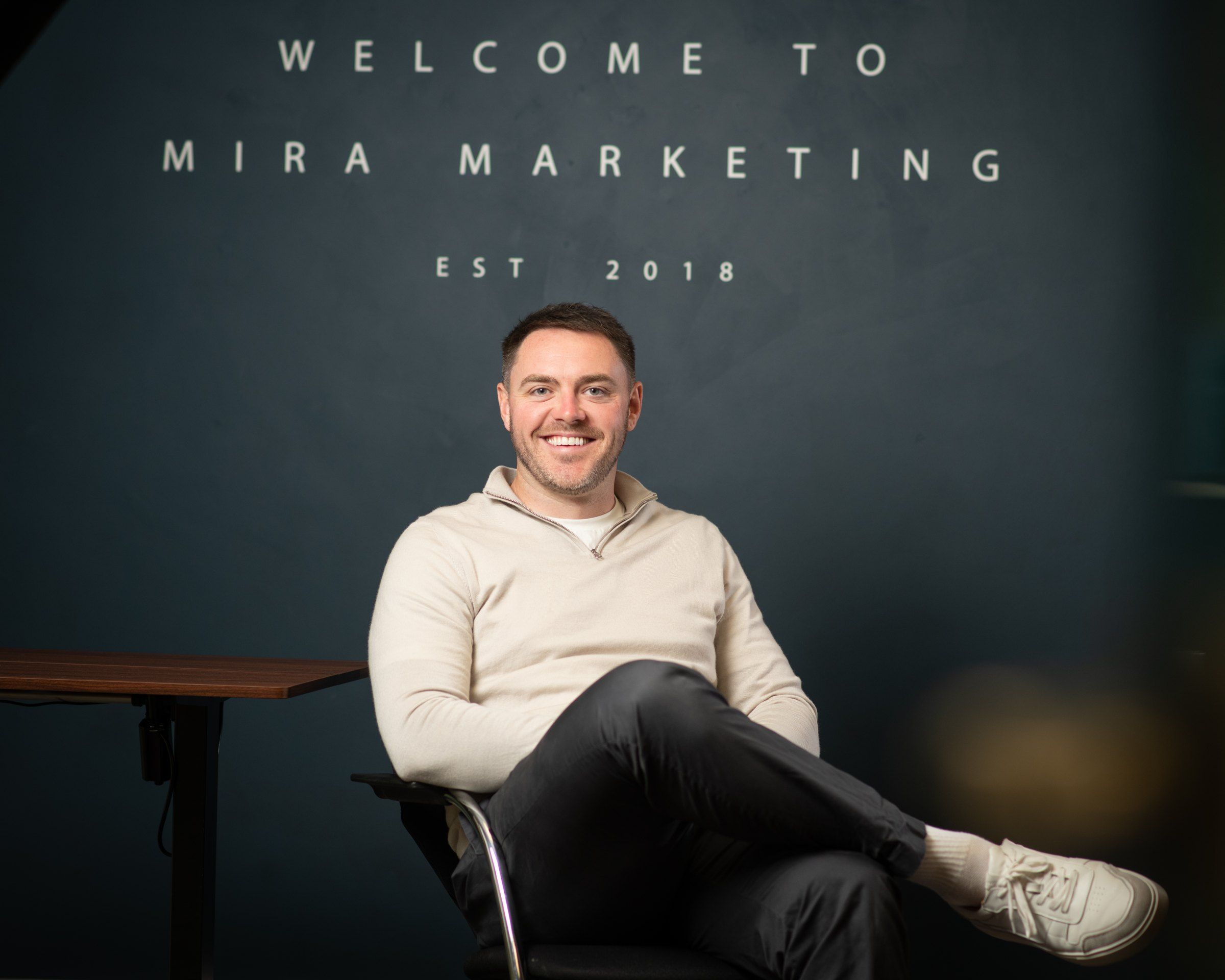 Stuart Bramley, Mira Marketing's founder, seated in front of the welcome wall in the agency's Newcastle office